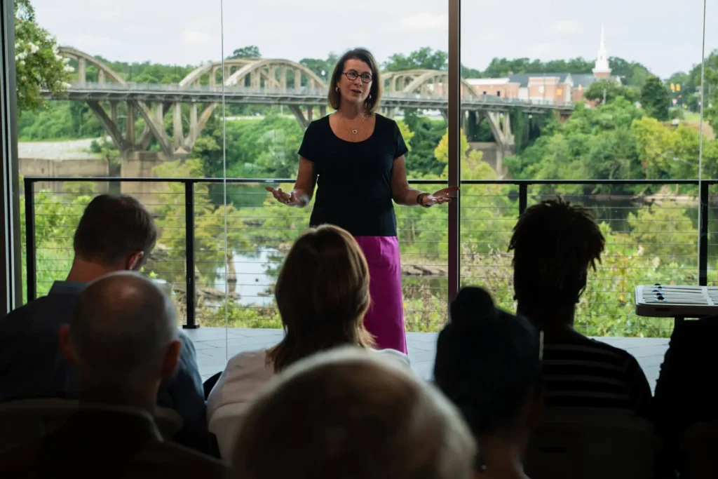 CACF Awards $123,640 in Education Grants to River Region Nonprofits 1 Burton speaking in front of a crowd in a room with a bridge in the background