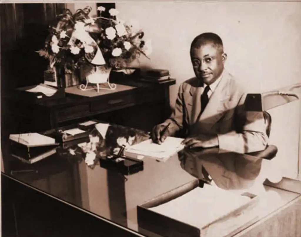 Dr. JF Drake seated at a desk